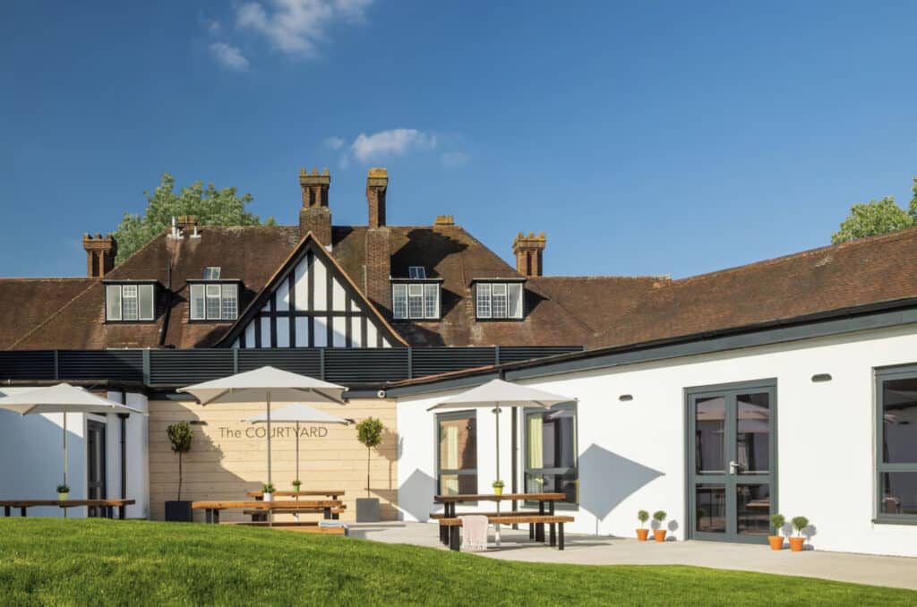 Hotellets fasade ute, grønt gress og blå himmel.