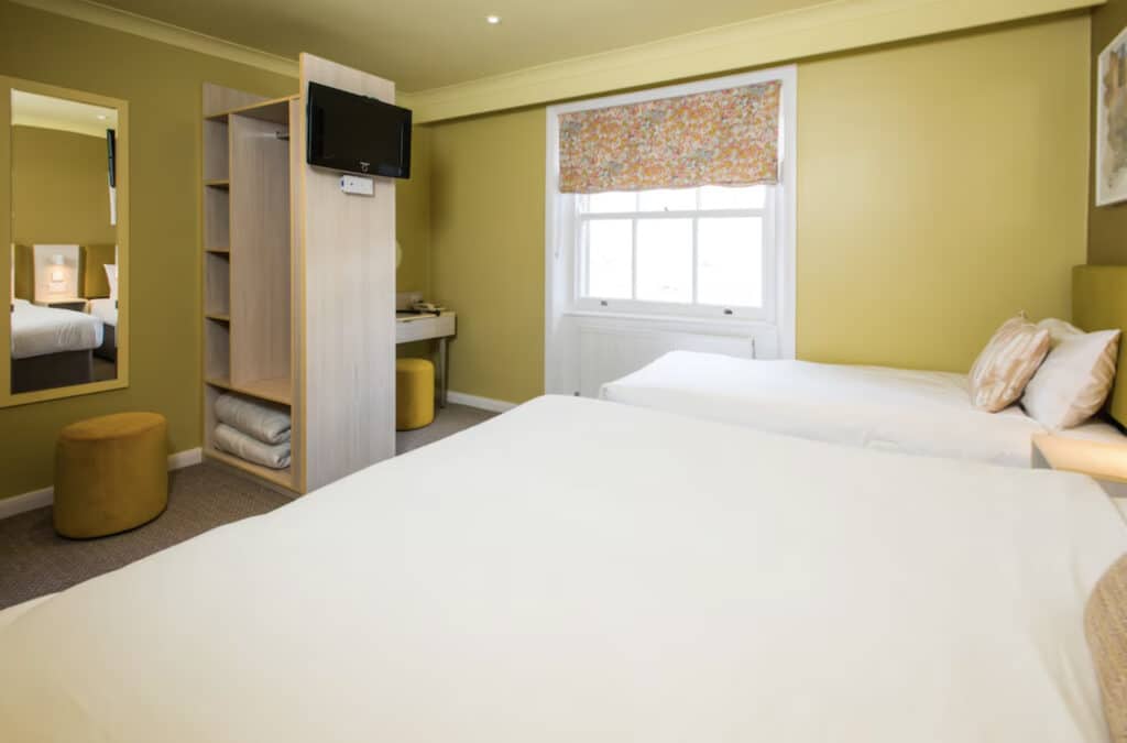 Hotellrom med to adskilte senger, liten TV på hylla, gule vegger.