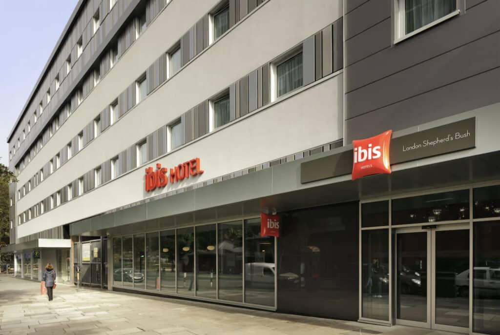 Hotellfasade med fortau og stort skilt i oransje.
