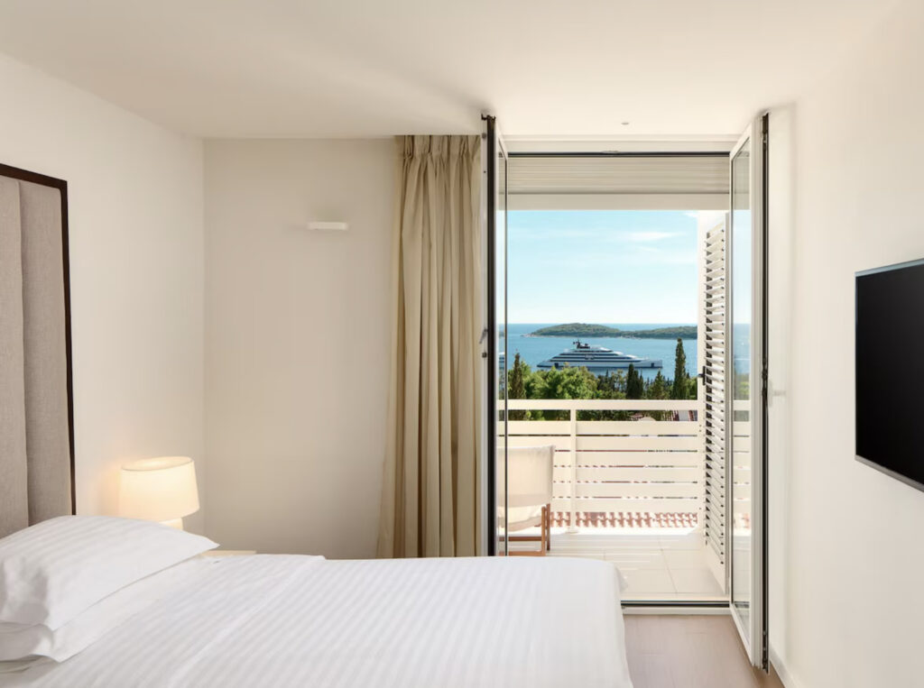 Hotellrom med dør som går til balkong, med utsikt over havet.