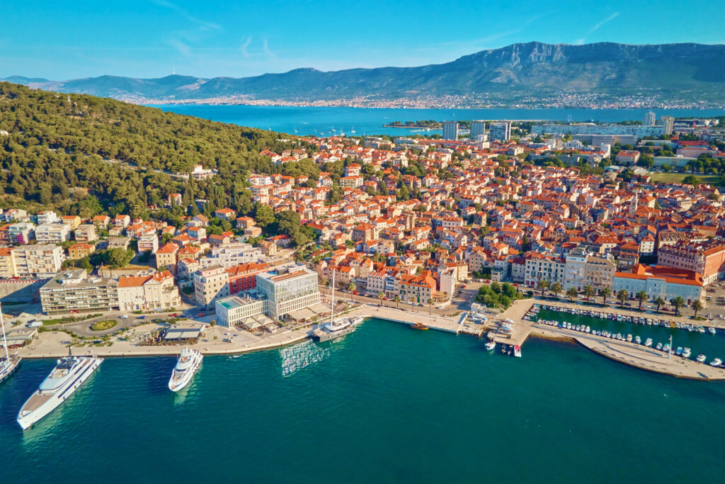 Luftfoto av Split, Kroatia. Bybilde av den kystnære turistbyen med havn og fjell i bakgrunnen. Gamlebyen består av historiske bygninger med røde takstein nær Adriaterhavet.