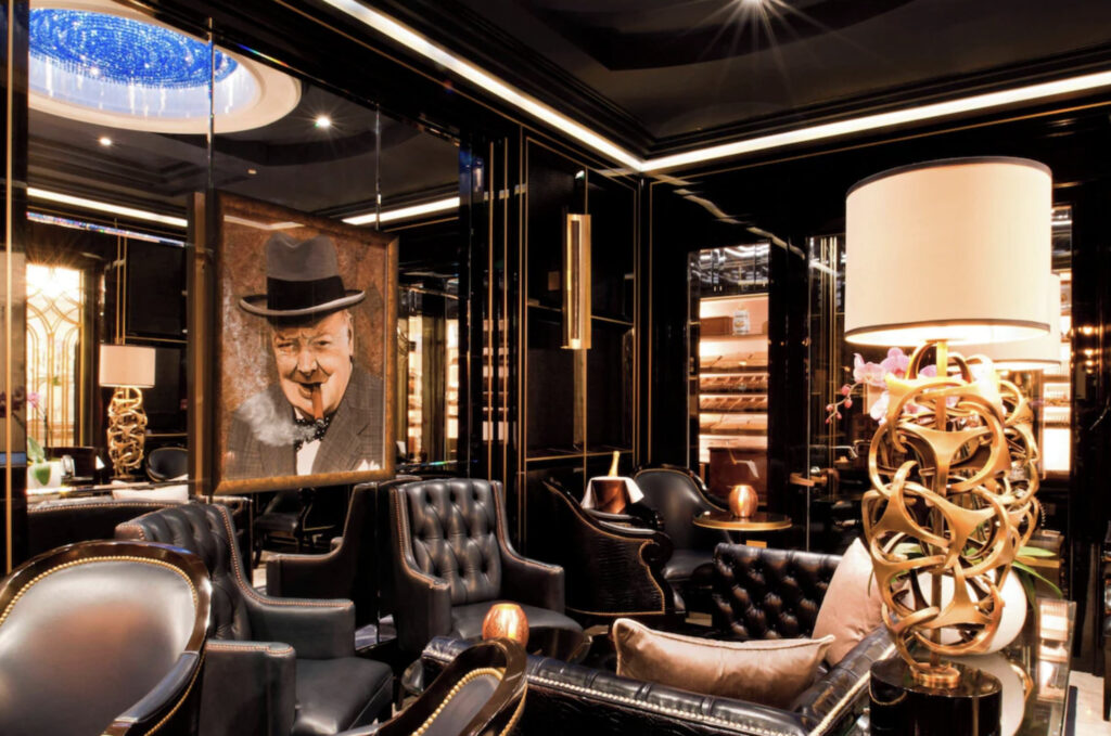 Lounge med bilde av en eldre mann med hatt og sigar i munn som smiler. Skinnstoler og hvit lampe. 