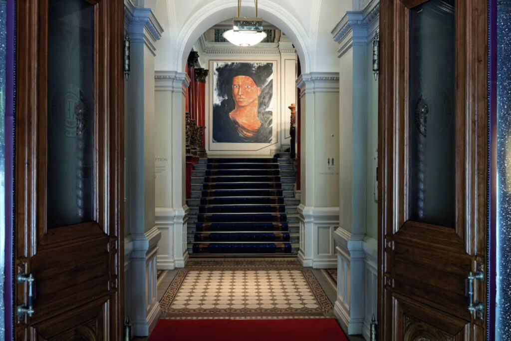 Inngang til hotellet med trapp og stort maleri på veggen av et ansikt.