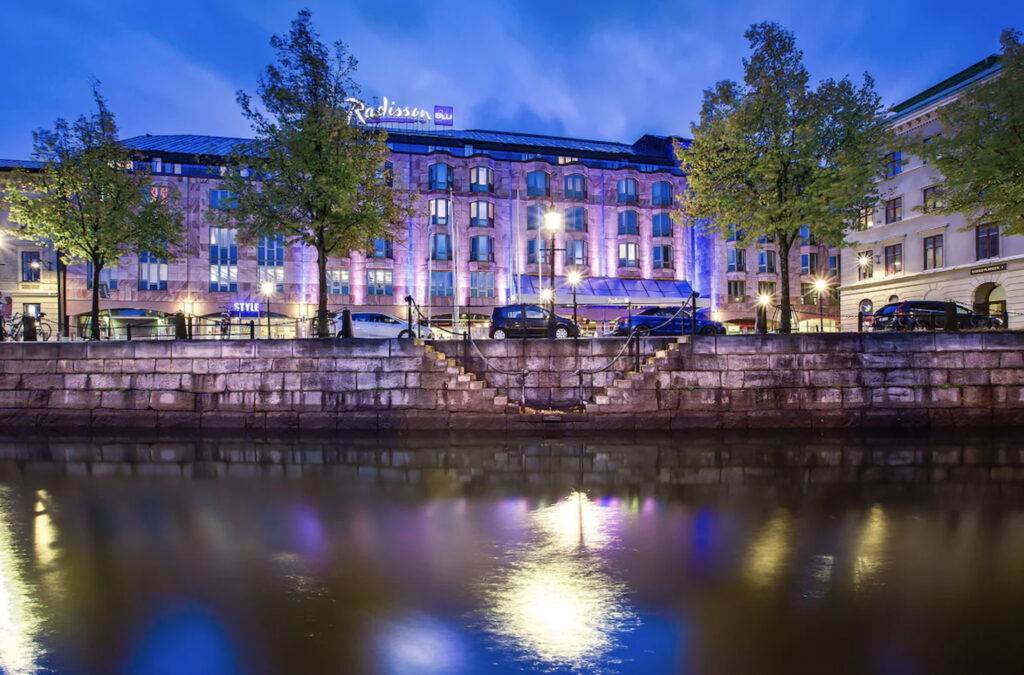 Hotellfasade med gatelys og elv foran.