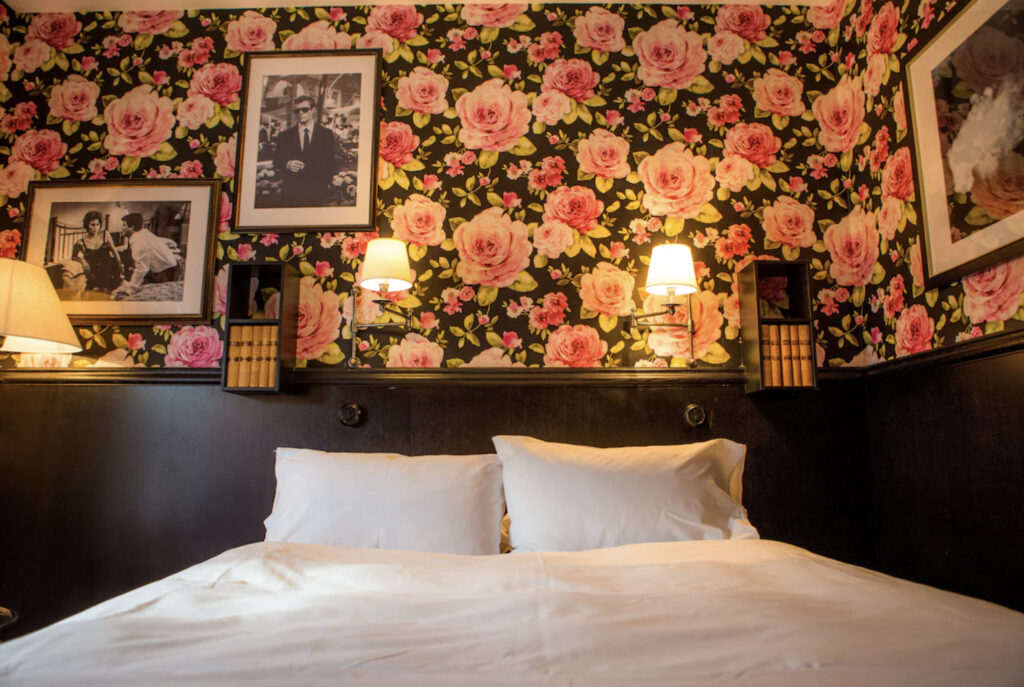 Hotellrom med dobbeltseng, rosetapet og gamle sort hvitt bilder på veggen.