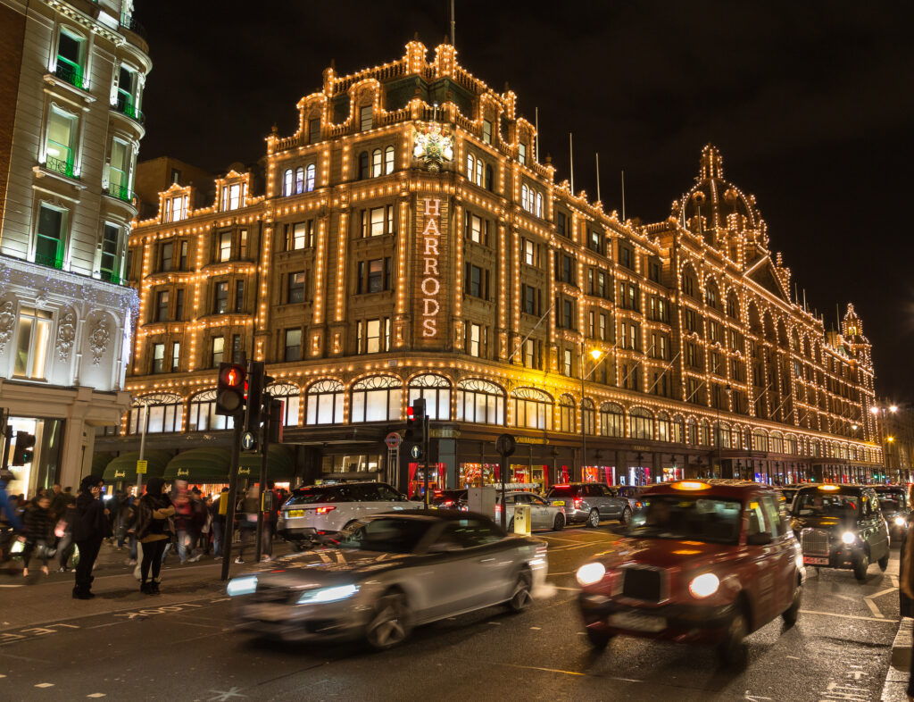 Utenfor Harrods varehus i London om kvelden i juletiden. Både mennesker og trafikk kan sees.