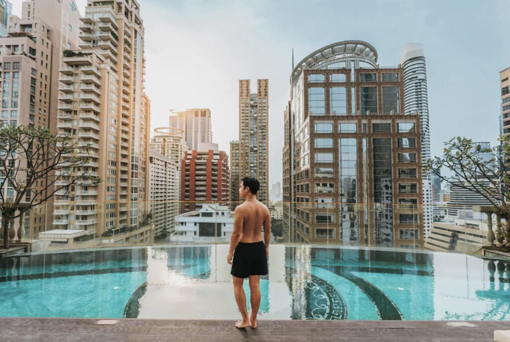 Mann som står ved bassengkanten utendørs. Utsikt mot høye bygninger.