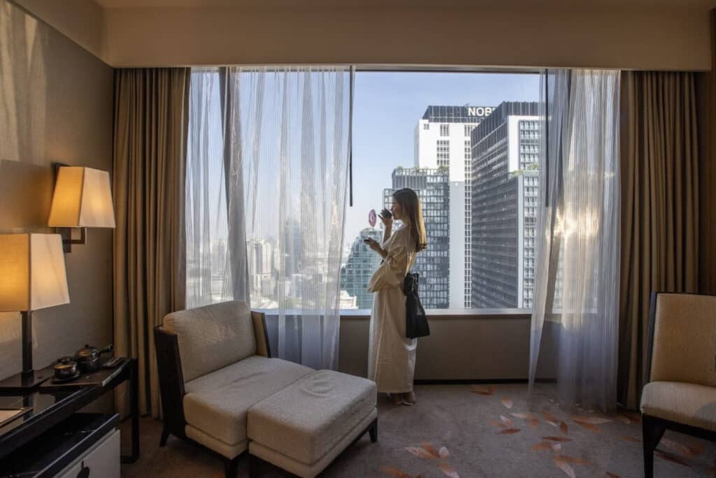 Dame som drikker kopp te og ser ut vinduet med utsikt over skyskrapere. 