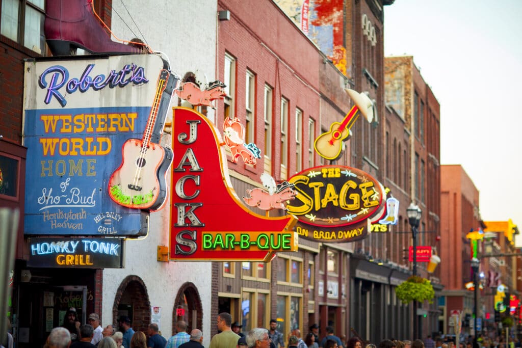 Mange neonlys-skilt med ulike navn på restauranter og barer. Gate med mennesker. 