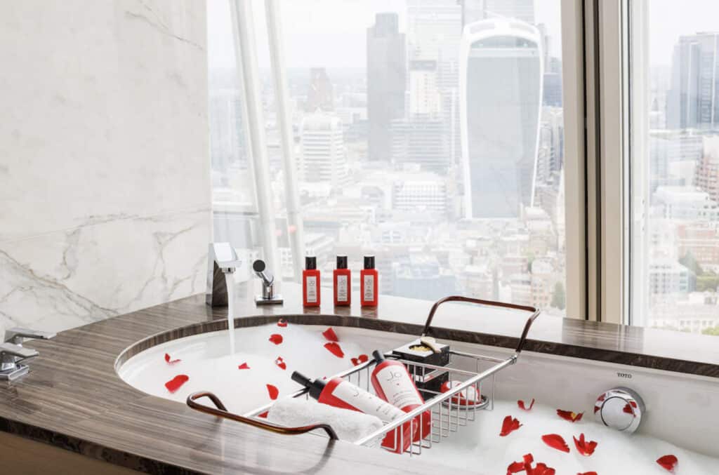 Badekar med roseblader,og røde shampoo og balsam. Med utsikt over London.