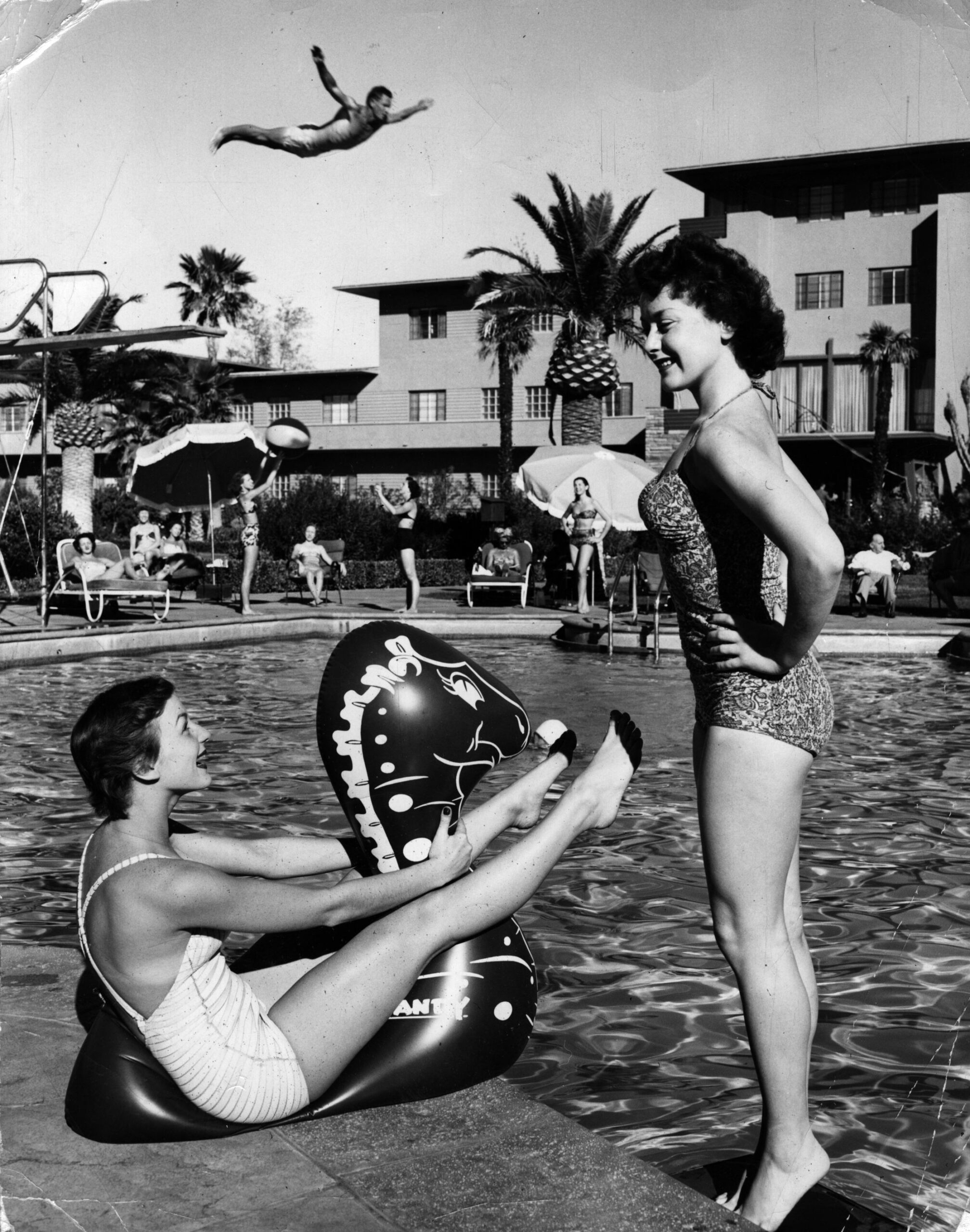 circa 1955: Two young women enjoying themselves by the pool at a Las Vegas holiday resort, while a man performs a spectacularly high dive in the background. (Photo by Keystone/Getty Images)