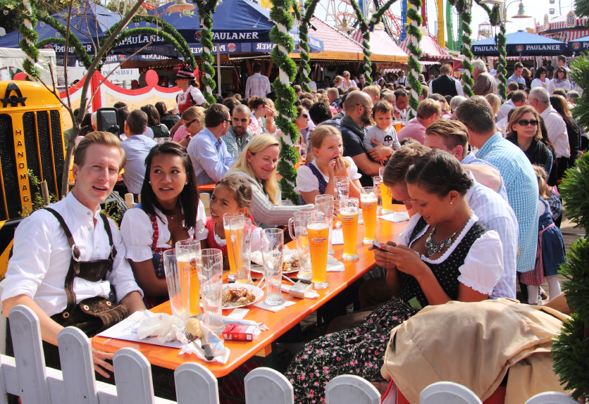 Young people in traditional costumes sitting in a beer garden on the Oktoberfest, Munich, Germany. They are having fun, drinking beer, enjoying themselves