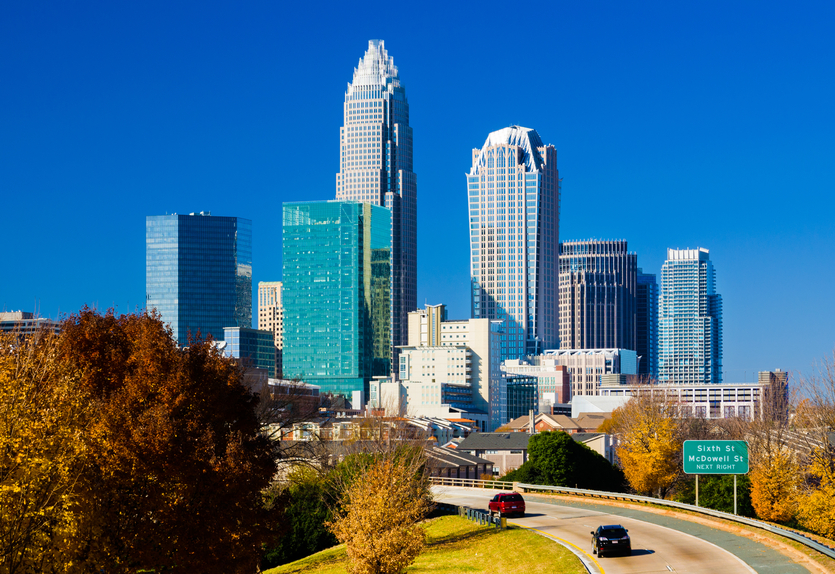 Downtown Charlotte skyline during Autumn with a highway onramp with cars in the foreground. Picture taken in a high contrast style with a deep blue sky.