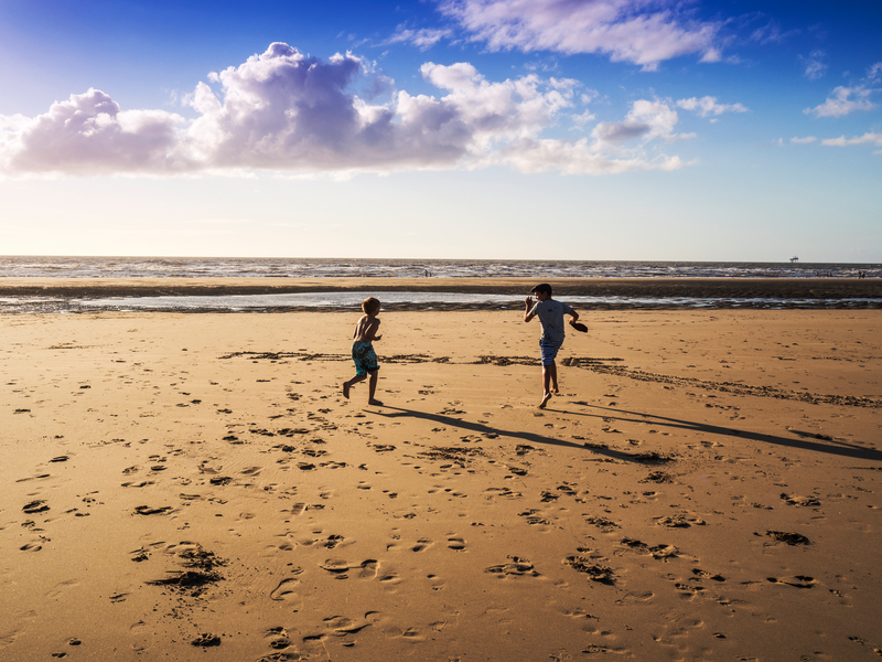 Two boys running on the beach in Formby, Merseyside, United Kingdom. An oil and gas drilling rig can be seen in the background in the Irish Sea.