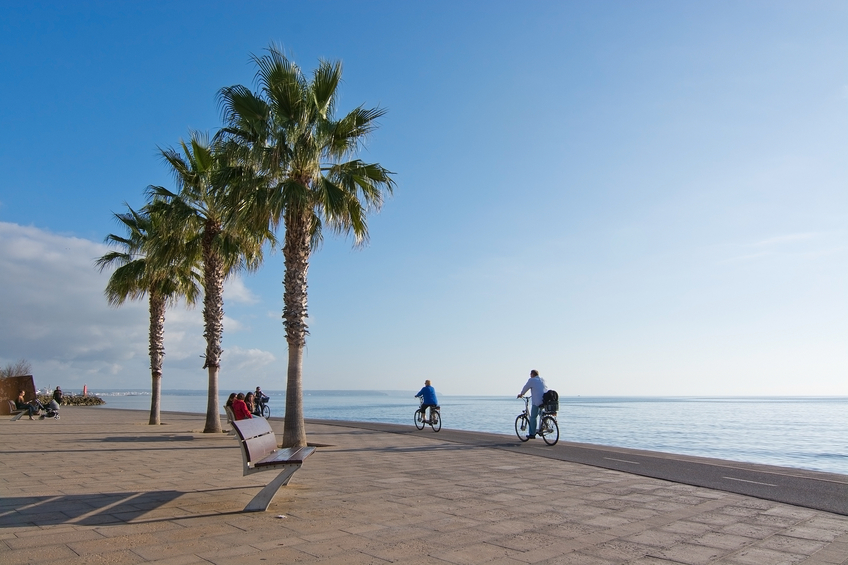 Palma de Mallorca, Balearic islands, Spain - December 22, 2015: People on bicycles travel on the Molinar boardwalk and bike track by the Mediterranean ocean in afternoon sunlight in December.