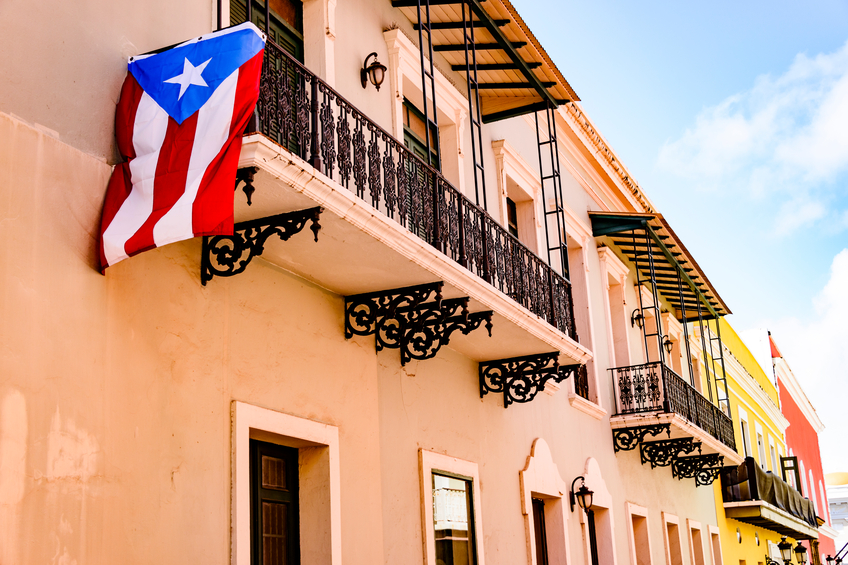 Colorful house facades along a street in Old San Juan, Puerto Rico with a Puerto Rican flag hanging down from one of the balconies