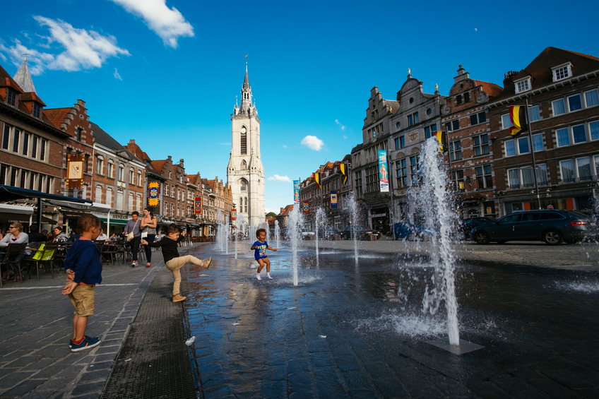 Tournai, Belgium - July 12, 2016: Three children play with a fountain at the Grand Place of the city, with the belfry (Beffroi) on the background.