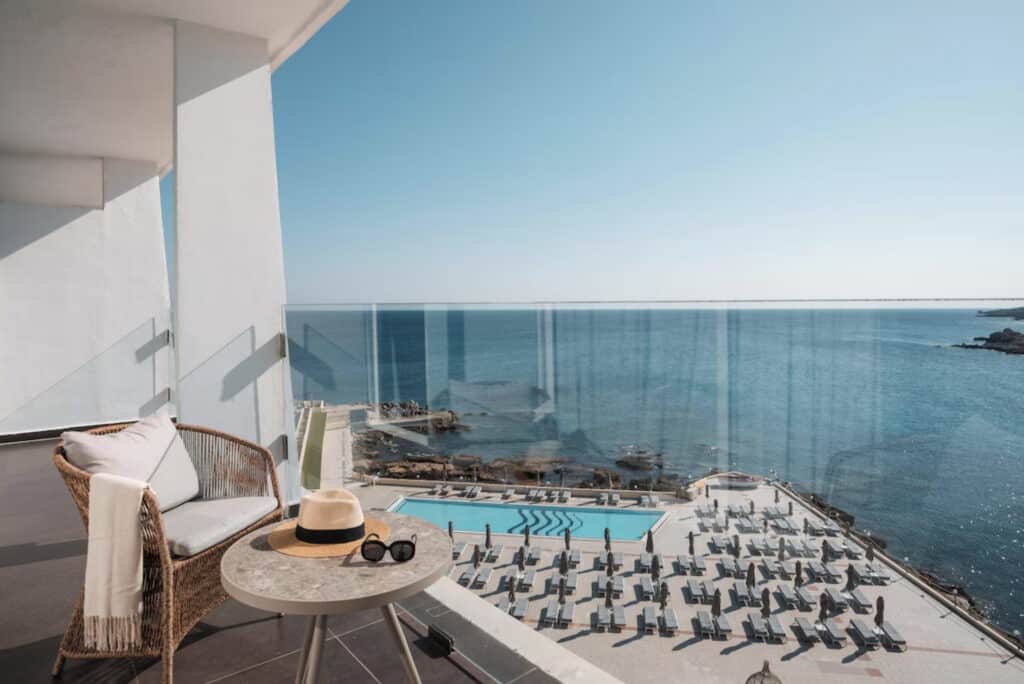 Hotellbalkong med sommerhatt, solbriller og utsikt over havet.