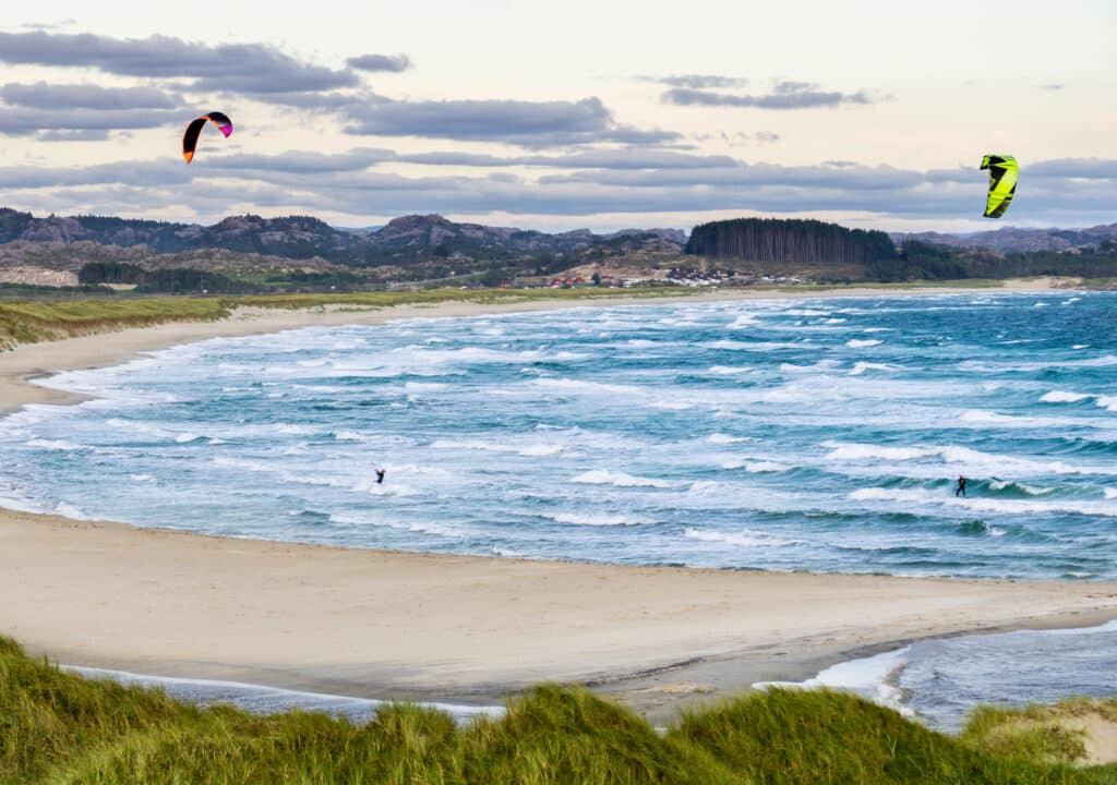 Brusand-strand i Norge, på Jæren. To kitesurfere i høye bølger på stranden.
