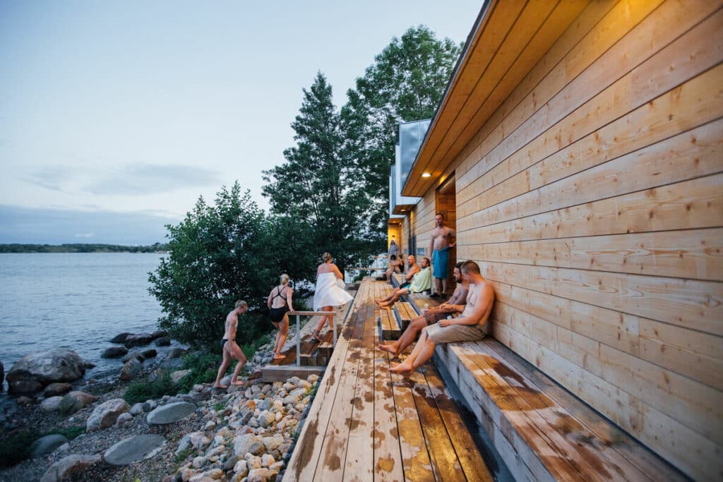 Sauna med mennesker utenfor som nyter utsikten mot vannet. Reis til FInland!