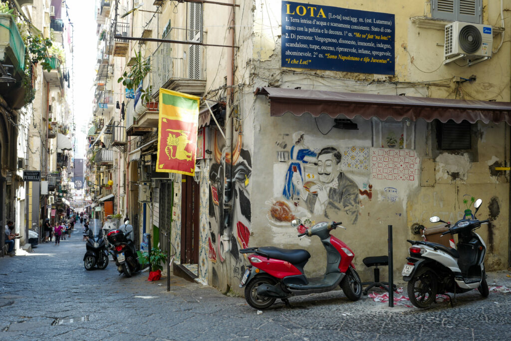 En smågate i Italia i Napoli med verdens beste pizza. Mopeder langs gaten, og folk. Bli med på ferie i Napolibukta.