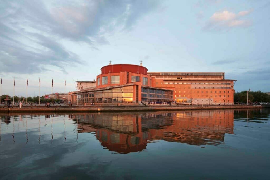 Operahus med oransje fasader ved vannet.