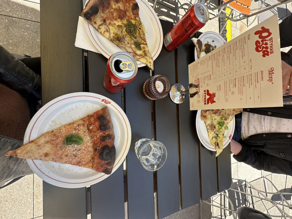 Tre stykker med pizza på bordet med Cola-boks.
