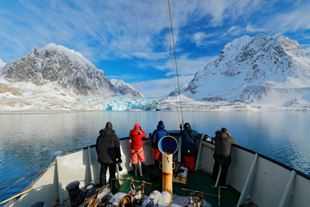 Svalbard, Longyearbyen i Norge. Fiskere og turister i båt, mot hvitt, snødekt vinterlandskap.