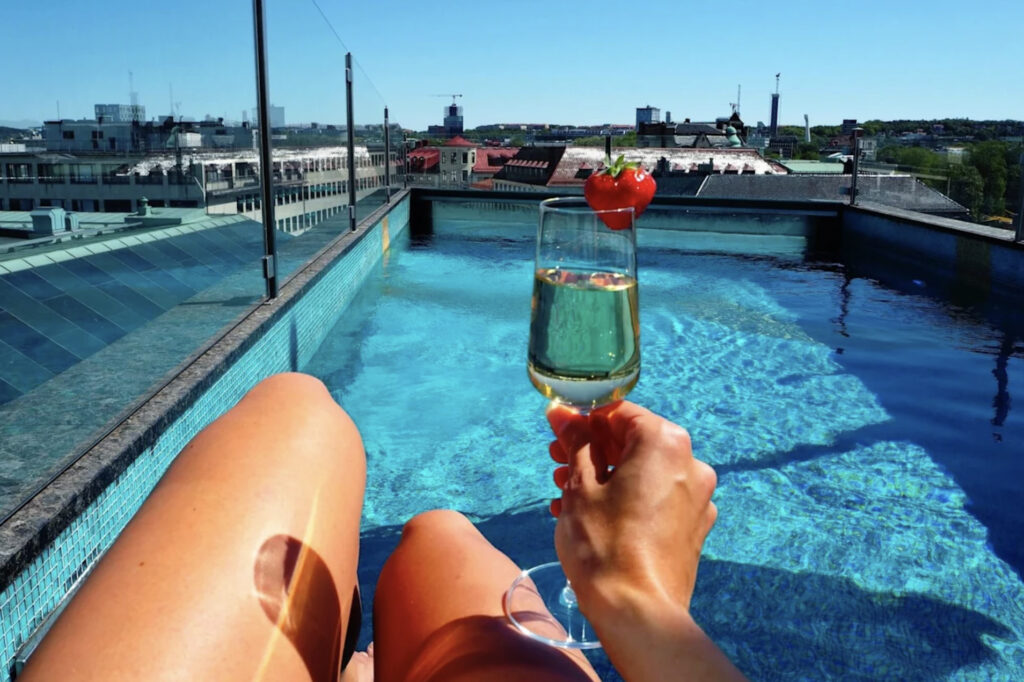 Takbasseng med kvinne som holder et champagneglass med jordbær med føttene i bassenget og ser ut over Stockholm by.