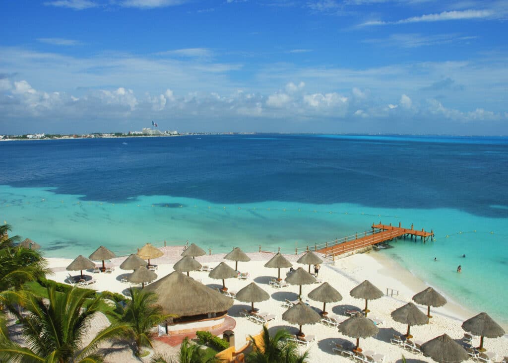 Cancun i Mexico med turkist vann, sand, palmer og brune parasoller.