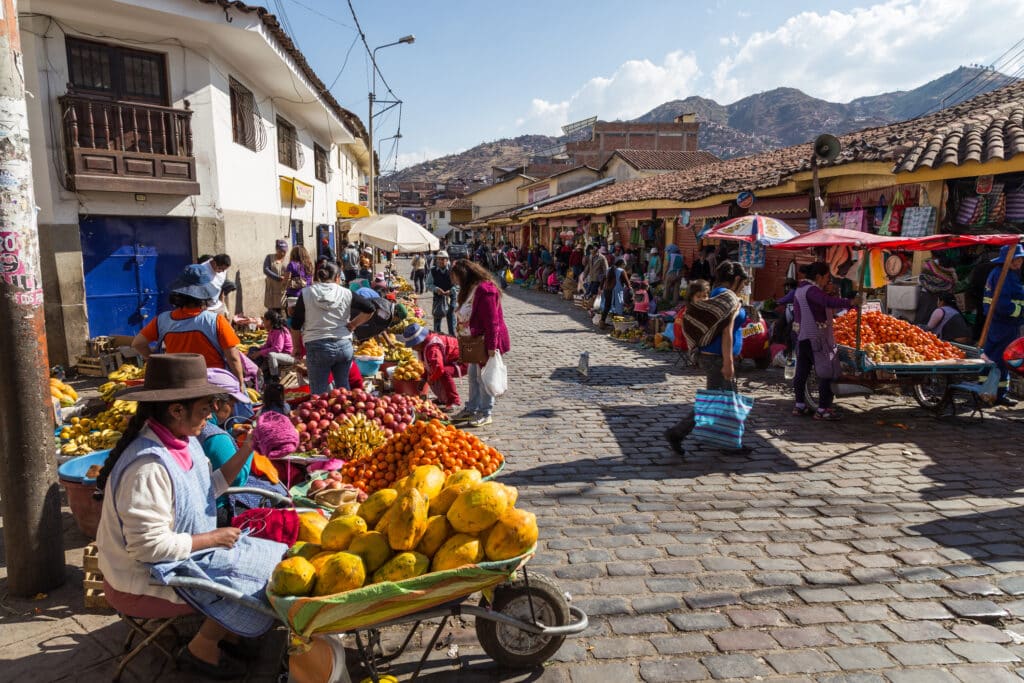 Markedsgate i Cusco i Peru, selgere som selger frukt i gatene. Damer med hatt og fargerike parasoller.