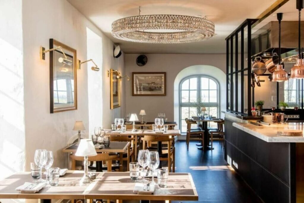Restaurant med stor lysekrone, gull-speil og hvite vegger.