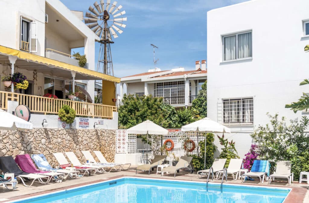 Eligonia hotell med basseng, hvit fasade og solsenger.