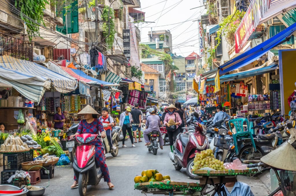 Hanoi i Vietnam med en dame i moped og folk i bakgrunnen med fruktmarked.