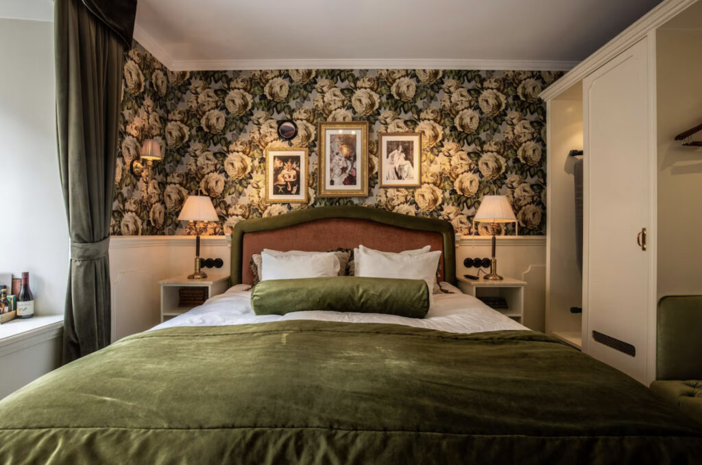 Hotellseng med grønn sengesett, mønstret vegger.