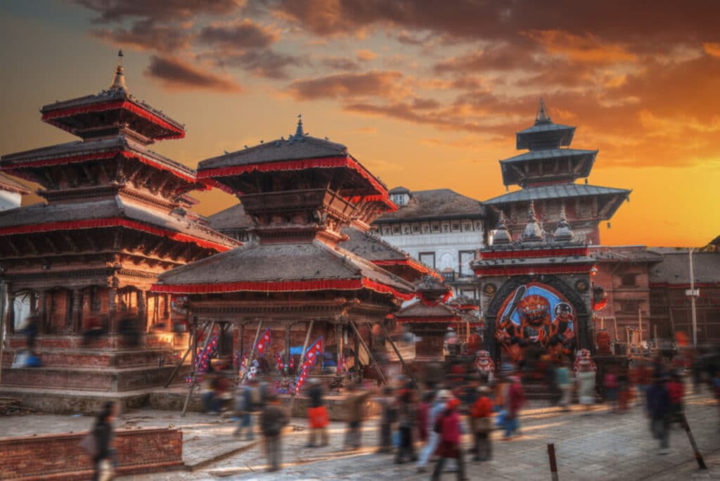 Katmandu i Nepal med fargerike bygninger, folkemengde og oransje solnedgang.