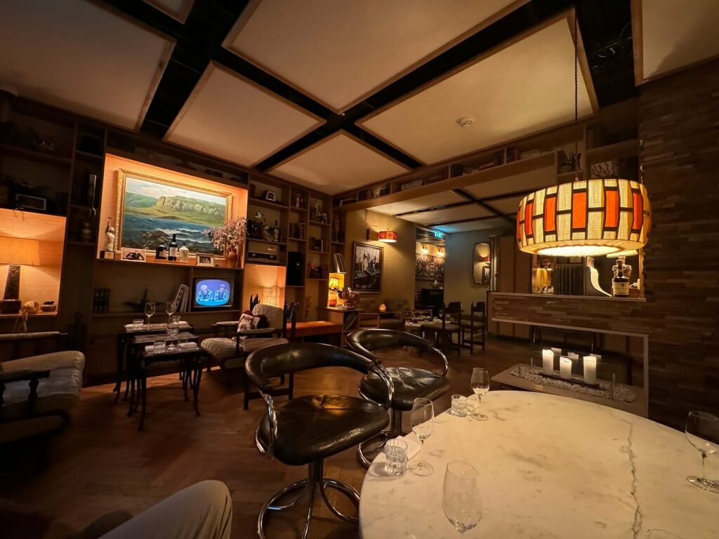 Restaurant med liten tv, brune vegger, maleri, og retro lampe og brune skinnstoler.
