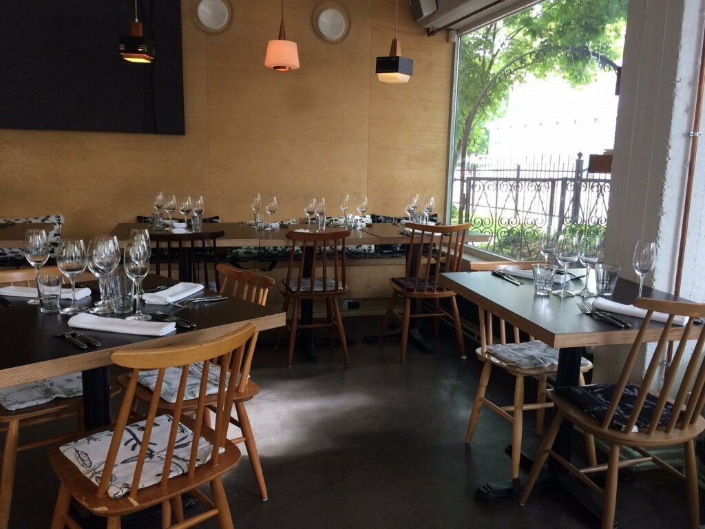 Restaurant med spisebord i tre, glass og enkelt design.