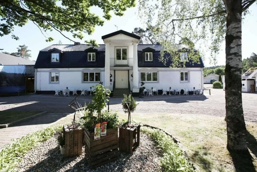 Signum i Sverige. Hotellfasade med gress, sitteplasser og hvit bygg.