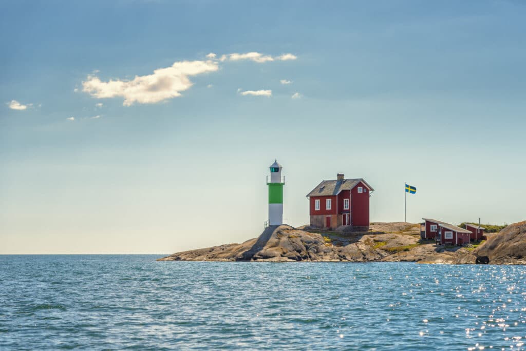 Sommersteder i Sverige. Rød hytte med svensk flagg i bakgrunnen, vann og blå himmel. 