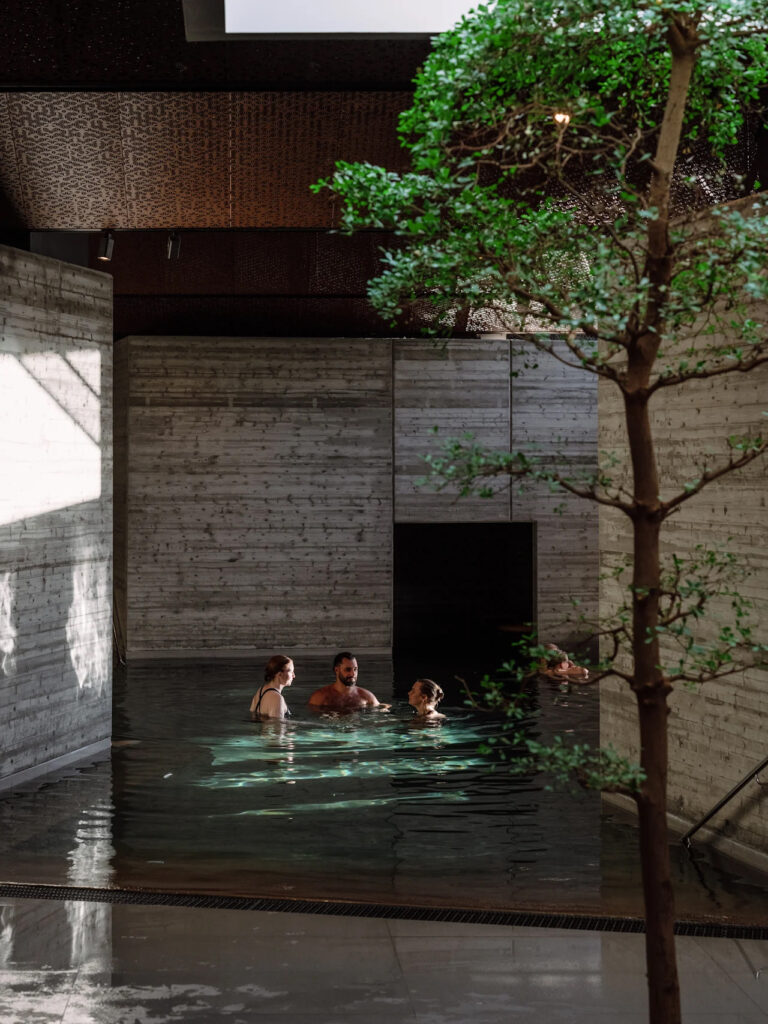 Hotellbasseng med bansai tre og folk i vannet. Trevegger som i Japan.