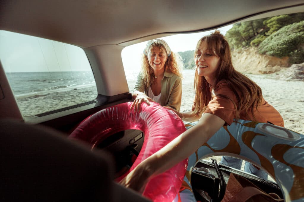 To glade damer på baksiden av bilen som henter ut baderinger og har parkert ved en strand.