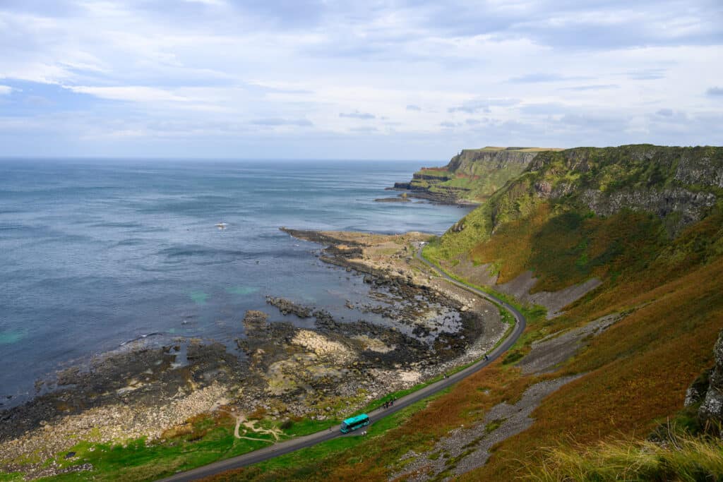 The Giant's Causeway Coast med bilvei og en buss som kjører på veien. Grønt fjell-landskap.