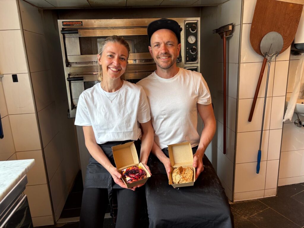 Paul og Kjersti Grønseth som viser fram bakeriene sine og smiler til kamera, rett foran bakeovnen på kjøkkenet. 