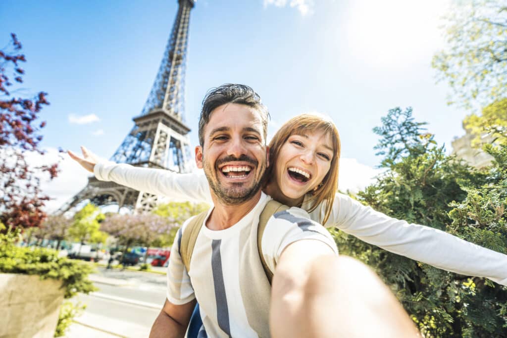 Kjærestepar foran Eiffeltårnet i Paris som poserer med stort smil og tar selfie.