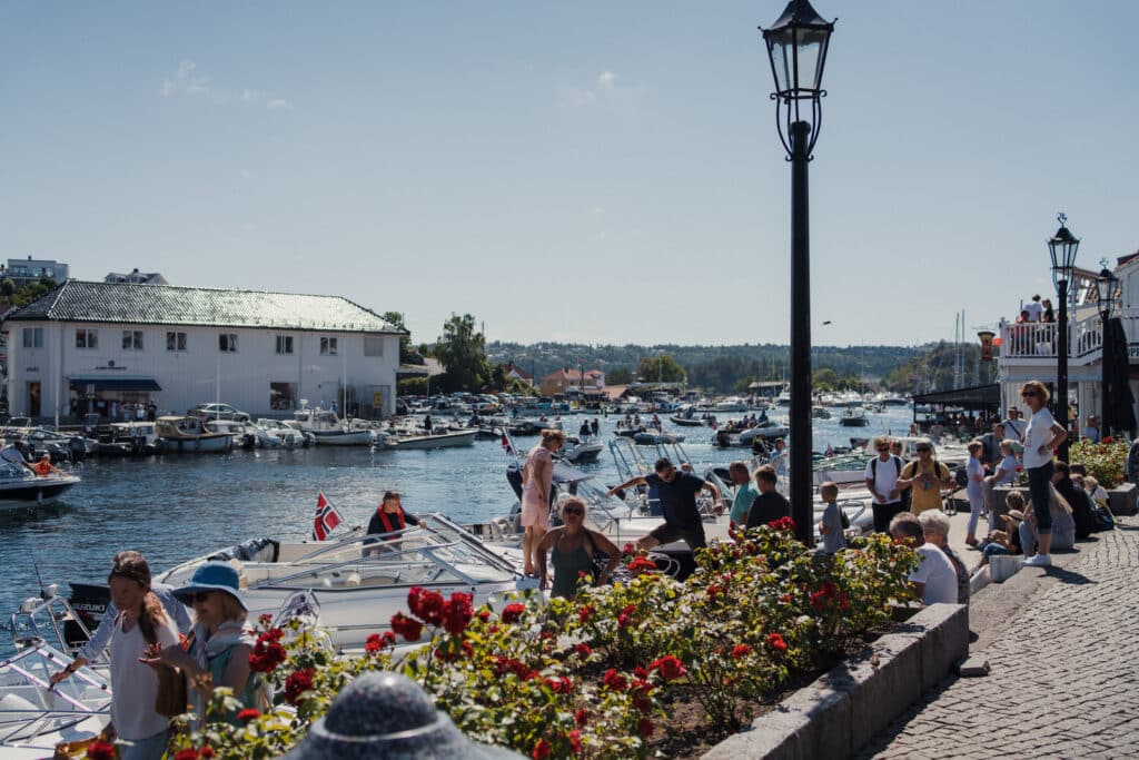 Kragerø ferie med folk som sitte rved bryggen og ser ut mot vannet. Båt, norsk flagg og roser langs.