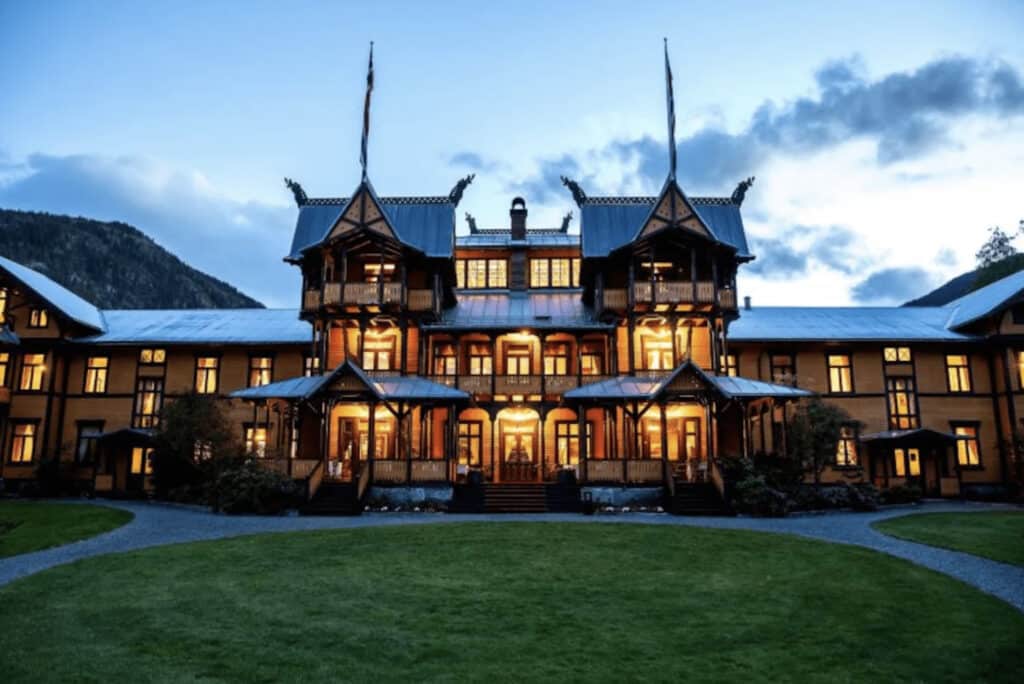 Hotellfasade, mørkt ute, grønt gress og lys fra innsiden.