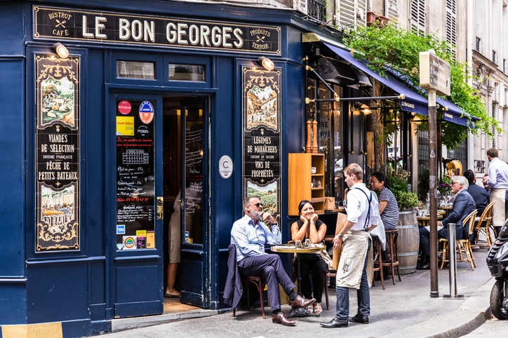 Gate i Paris med kafeer og folk som sitter ute og prater. 