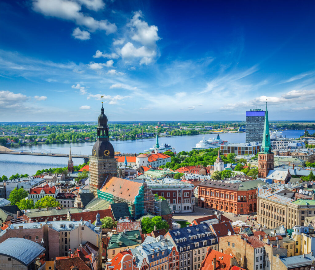 Riga by med båt, vann, gamle bygninger og blå himmel.