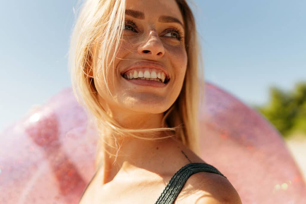 Dame som smiler stort med badering på stranden. 